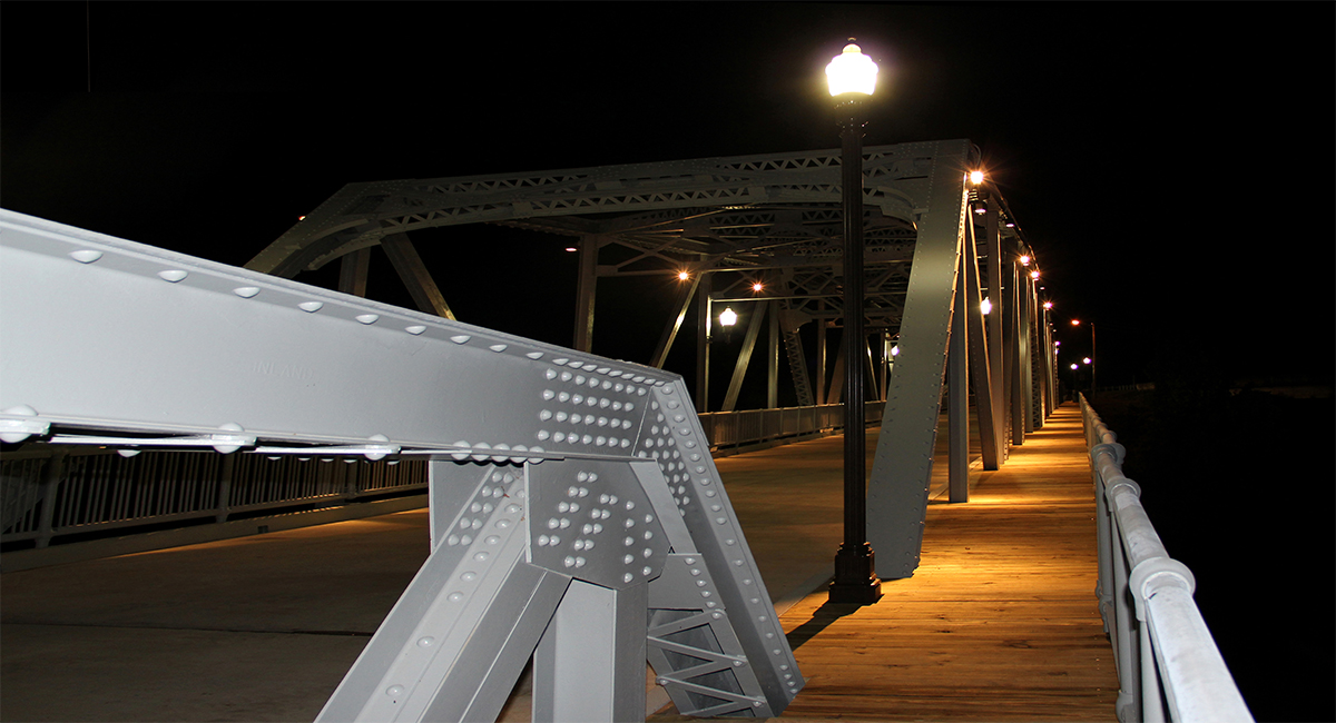 Lampposts lit up on the side of a bridge at night.